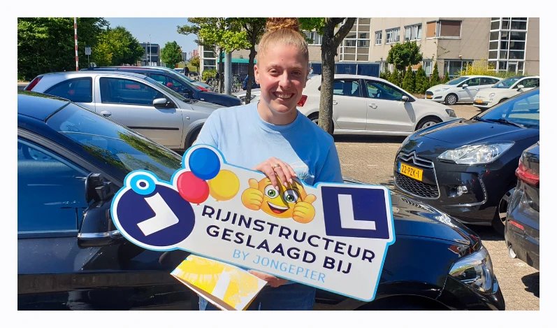 Geslaagde vrouwelijke cursist houdt een bord vast met de tekst “Rijinstructeur geslaagd bij Jongepier” na afronding van de rijinstructeur opleiding